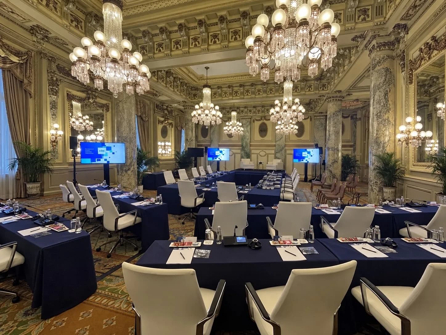 Board meeting tables set inside an ornate room with chandeliers