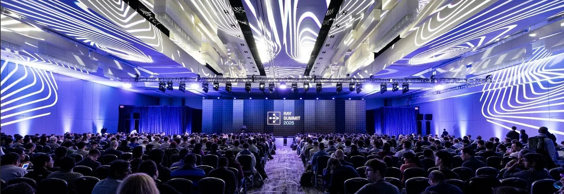 A large conference audience beneath an illuminated ceiling